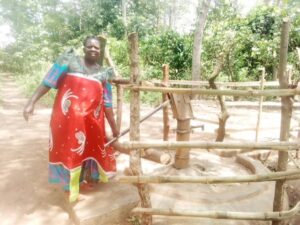 Borehore surrounded by wooden frames, with a woman pumping water